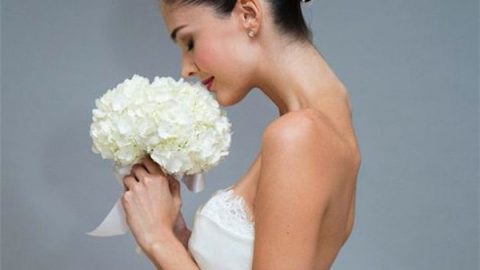 تسريحة الكعكة المعقودة بشريطة بيضاء بها وردة للعروس من Carolina Herrera ربيع 2015